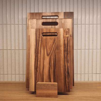 Set of wooden cutting boards with handles against a tiled wall.