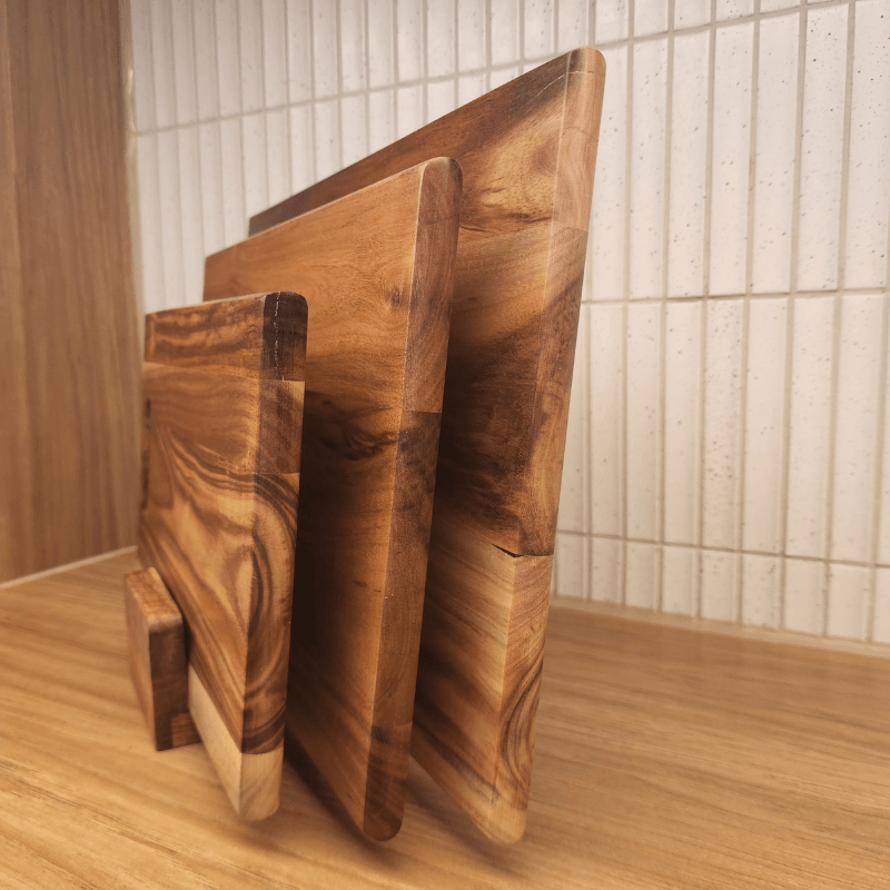 Three wooden cutting boards of different sizes on a wooden surface with a tiled wall background.