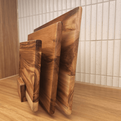 Three wooden cutting boards of different sizes on a wooden surface with a tiled wall background.