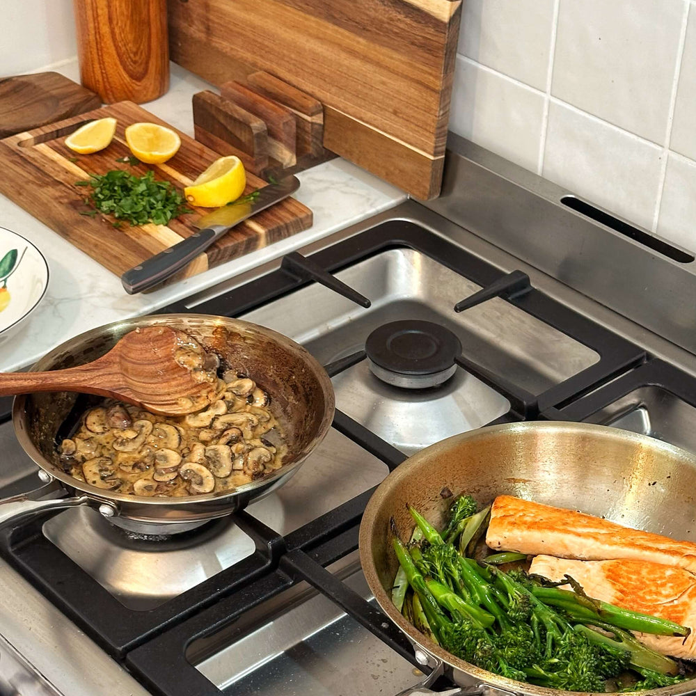 Stovetop with two pans containing food, surrounded by kitchen utensils and ingredients.