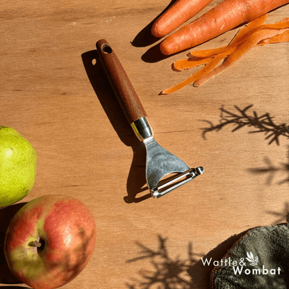 Peeler on a wooden surface with carrots and apples, featuring the brand 'Wattle & Wombat'.