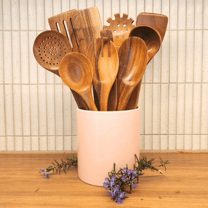 Set of wooden kitchen utensils in a pink holder on a wooden surface with a tiled wall background.